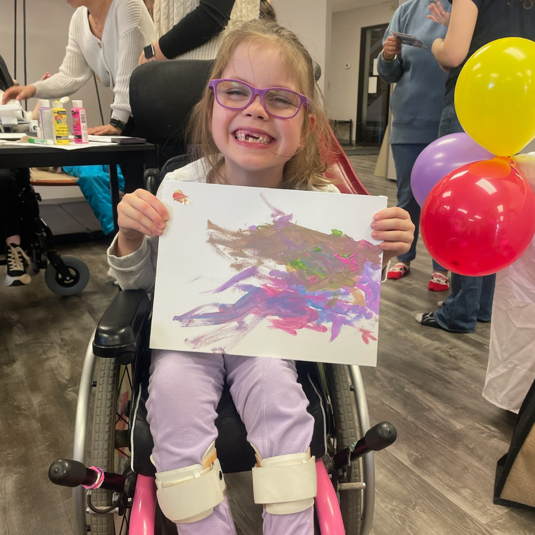 Picture of little girl in wheelchair holding up the art she created with Guided Hands
