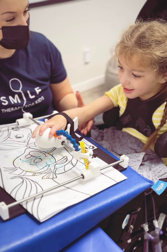 Little girl in wheelchair using Guided Hands to colour a picture of a fish